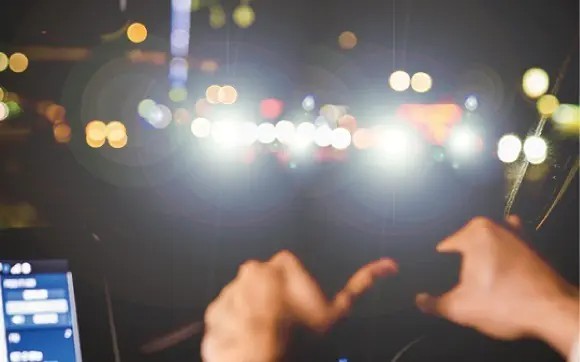 車のヘッドライトで非常にまぶしい夜の街並みでの運転シーン